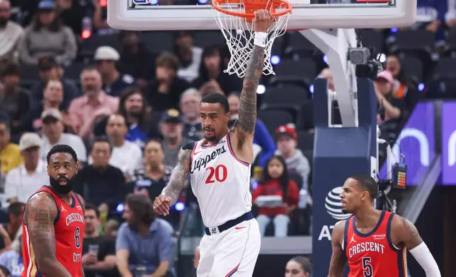 Los Angeles Clippers forward John Collins (20) hangs on the basket after dunking as New Orleans Pelicans guard Dejounte Murray (5) watches and center DeAndre Jordan (6) looks on during the first half of an NBA basketball game, Sunday, March 1, 2026, in Inglewood, Calif. (AP Photo/Jessie Alcheh)
