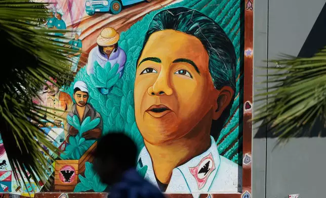 A pedestrian walks below an image of César Chavez on a mural in San Francisco, Wednesday, March 18, 2026. (AP Photo/Jeff Chiu)