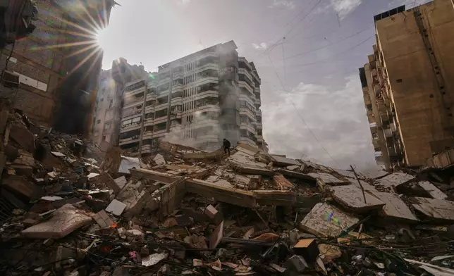 A man stands atop the rubble as smoke rises from a building destroyed in an Israeli airstrike in Dahiyeh, Beirut's southern suburbs, Lebanon, Saturday, March 14, 2026. (AP Photo/Hassan Ammar)