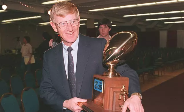 FILE - Notre Dame head coach Lou Holtz carries away the National College Champion Trophy following a news conference in Tempe, Ariz. in this Jan. 3, 1989 photo. (AP Photo/Rob Schmacher, File)