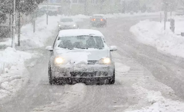 A car drives down a snow-covered street during heavy snowfall in in Bihac, Bosnia, Friday, March 27, 2026. (AP Photo/Edvin Zulic)
