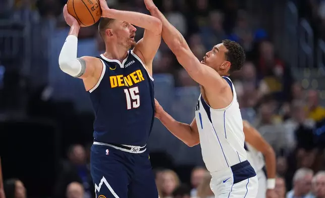 Denver Nuggets center Nikola Jokić, left, looks to pass the ball as Dallas Mavericks forward Dwight Powell defends in the first half of an NBA basketball game Wednesday, March 25, 2026, in Denver. (AP Photo/David Zalubowski)