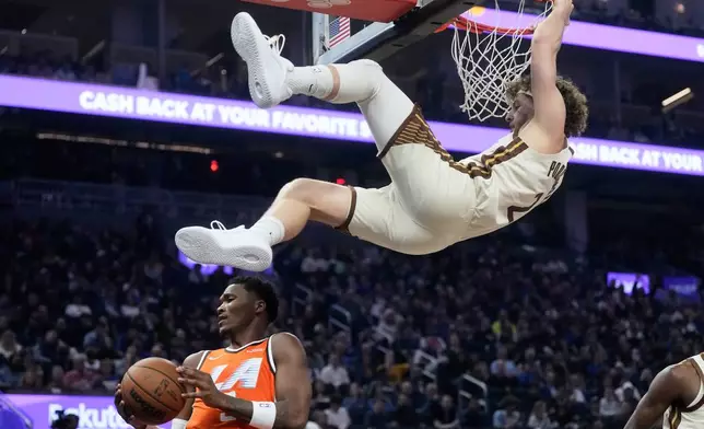Golden State Warriors guard Brandin Podziemski, top, hangs onto the rim over Los Angeles Clippers guard Bennedict Mathurin after dunking during the first half of an NBA basketball game in San Francisco, Monday, March 2, 2026. (AP Photo/Jeff Chiu)