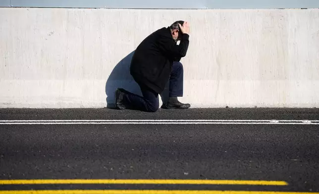A man takes cover by the side of the road as an air raid sirens warn of incoming Iranian missile strikes in Tel Aviv, Israel, March 17, 2026. (AP Photo/Ohad Zwigenberg)