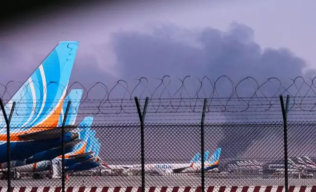 FlyDubai planeS is parked at Dubai International Airport as smoke rises in the background after a drone struck a fuel tank early morning, forcing the temporary suspension of flights, in Dubai, United Arab Emirates, Monday, March 16, 2026. (AP Photo)