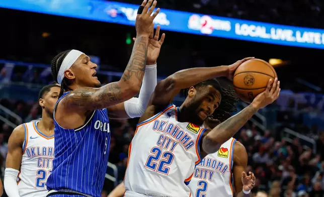 Oklahoma City Thunder guard Cason Wallace (22) pulls down a rebound around Orlando Magic forward Paolo Banchero, left, during the first half of an NBA basketball game, Tuesday, March 17, 2026, in Orlando, Fla. (AP Photo/Kevin Kolczynski)