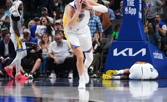 Golden State Warriors center Kristaps Porzingis, center, and guard Gary Payton II, left, react after guard Moses Moody (4) suffered an injury during overtime of an NBA basketball game against the Dallas Mavericks Monday, March 23, 2026, in Dallas. (AP Photo/Julio Cortez)