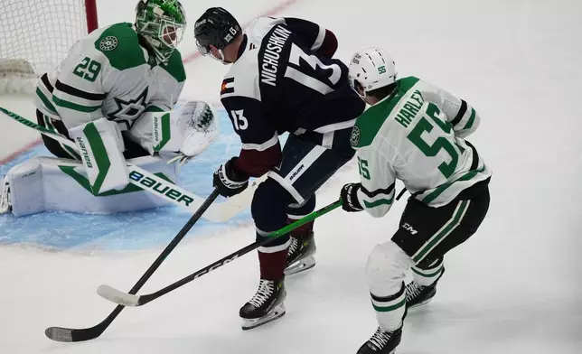 Colorado Avalanche right wing Valeri Nichushkin, center, drives past Dallas Stars defenseman Thomas Harley, right, to put a shot on goaltender Jake Oettinger in the first period of an NHL hockey game, Wednesday, March 18, 2026, in Denver. (AP Photo/David Zalubowski)