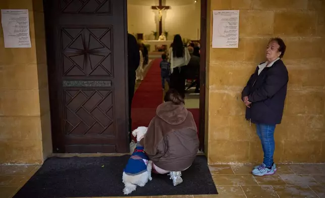 A Catholic woman kneels beside her dog at the entrance of a church during a Palm Sunday Mass in Beirut, Lebanon, Sunday, March 29, 2026. (AP Photo/Emilio Morenatti)