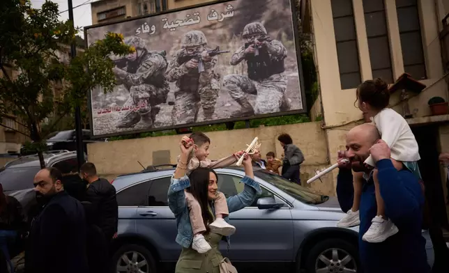 Catholic worshipers carry their children on their shoulders as they march in a procession during a Palm Sunday Mass in Beirut, Lebanon, Sunday, March 29, 2026. The poster in the background reads in Arabic: "Honor, sacrifice and loyalty". (AP Photo/Emilio Morenatti)