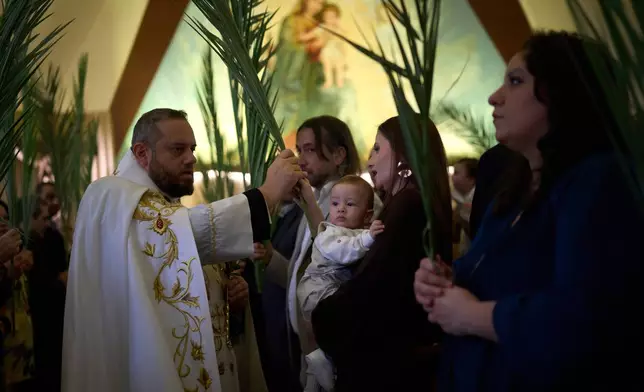 A priest blesses the palm branches held by the worshippers during a Palm Sunday Mass at the Our Lady of Hadat Church in Beirut, Lebanon, Sunday, March 29, 2026. (AP Photo/Emilio Morenatti)