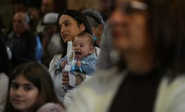 A woman holds her baby as people attend Palm Sunday Mass at Saint Thomas Cathedral, in the southern port city of Tyre, south Lebanon, Sunday, March 29, 2026. (AP Photo/Hussein Malla)