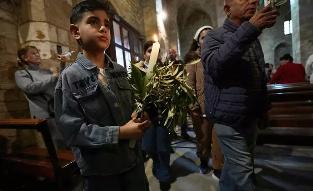 A boy holds a candle during Palm Sunday Mass procession at Saint Thomas Cathedral, in the southern port city of Tyre, south Lebanon, Sunday, March 29, 2026. (AP Photo/Hussein Malla)