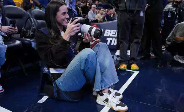 Indiana Fever guard Caitlyn Clark takes photos during pregame before an NBA basketball game between the Indiana Pacers and the Los Angeles Lakers in Indianapolis, Wednesday, March 25, 2026. (AP Photo/Michael Conroy)