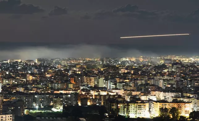 In this photo taken with a slow shutter speed, a Middle East Airlines plane flies over Beirut as smoke rises from Israeli airstrikes on Dahiyeh in Beirut's southern suburbs, early Monday, March 2, 2026. (AP Photo/Hassan Ammar)