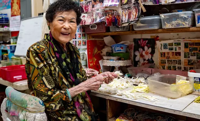 Cindy Lau, owner of Cindy's Lei Shoppe, poses for a portrait as she threads flowers onto string in Chinatown, Thursday, Feb. 26, 2026, in Honolulu. (AP Photo/Mengshin Lin)