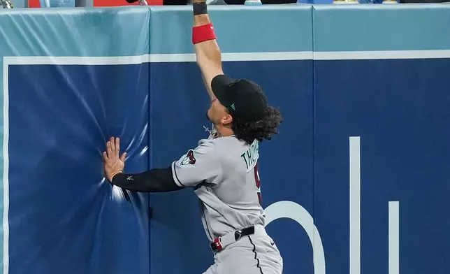 Arizona Diamondbacks center fielder Alek Thomas (5) leaps for the ball as it goes over the wall for a home run by Los Angeles Dodgers Mookie Betts (50) during the third inning of a baseball game Friday, March 27, 2026, in Los Angeles. (AP Photo/Caroline Brehman)