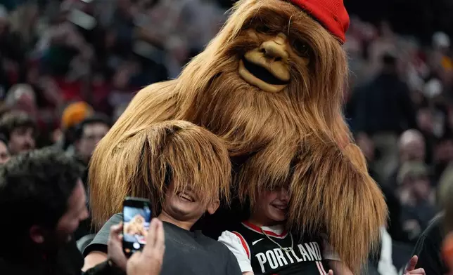 Fans pose for a photo with the mascot Douglas Fur during the first half of an NBA basketball game between the Portland Trail Blazers and the Utah Jazz, Friday, March 13, 2026, in Portland, Ore. (AP Photo/Jenny Kane)