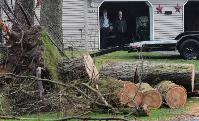 An uprooted tree is cut in the aftermath of a powerful storm that ripped through the area a day earlier in Lake Village, Ind., Wednesday, March 11, 2026. (AP Photo/Nam Y. Huh)