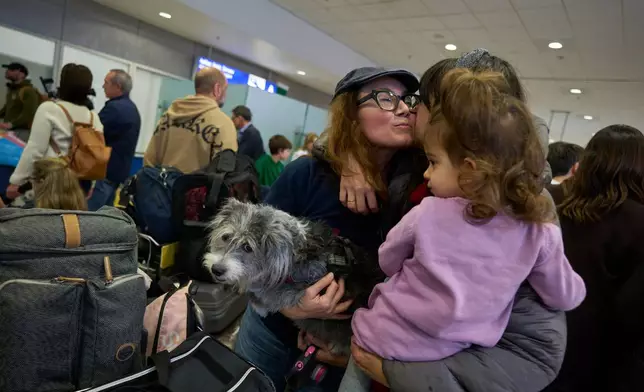 A repatriated Greek woman with her dog hugs relatives during their arrival at Athens International Airport Eleftherios Venizelos on Wednesday, March 18, 2026, after being evacuated from Abu Dhabi amid the escalating U.S.-Israeli conflict with Iran. (AP Photo/Petros Giannakouris)