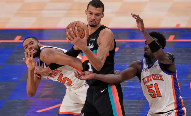 New York Knicks' Mikal Bridges, left, fouls San Antonio Spurs' Victor Wembanyama, center, while Bridges and Mohamed Diawara (51) try to get to the ball during the second half of an NBA basketball game Sunday, March 1, 2026, in New York. (AP Photo/Seth Wenig)