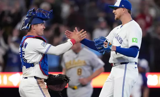 Toronto Blue Jays pitcher Jeff Hoffman (23) celebrates with teammate Toronto Blue Jays catcher Tyler Heineman, left, after defeating the Athletics during the ninth inning of an American League baseball game, in Toronto, Sunday, March 29, 2026. (Nathan Denette/The Canadian Press via AP)