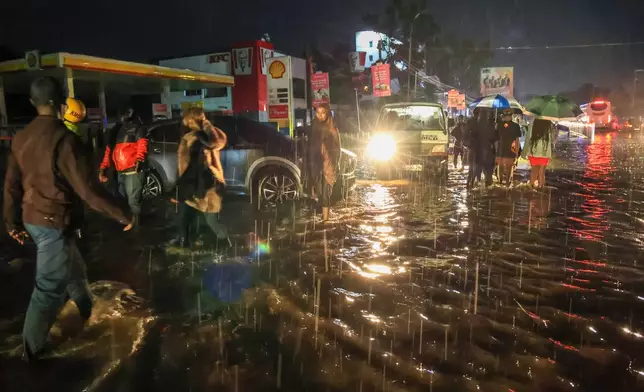 People walk through floodwaters after heavy rains in Nairobi, Kenya, on Saturday, March 7, 2026. (AP Photo/Andrew Kasuku)