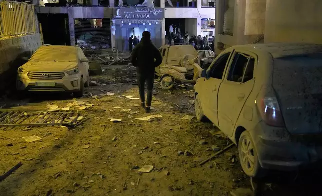 A man walks at the site of a destroyed branch of Al-Qard Al-Hassan, background, a non-bank financial institution run by Hezbollah, which was hit by an Israeli airstrike in central Beirut, Lebanon, Thursday, March 12, 2026. (AP Photo/Hussein Malla)