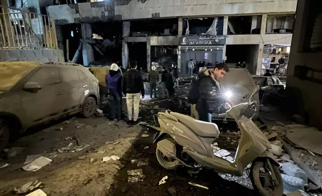 A man checks his scooter near a destroyed branch of Al-Qard Al-Hassan, background, a non-bank financial institution run by Hezbollah, which was hit by an Israeli airstrike in central Beirut, Thursday, March 12, 2026. (AP Photo/Hussein Malla)