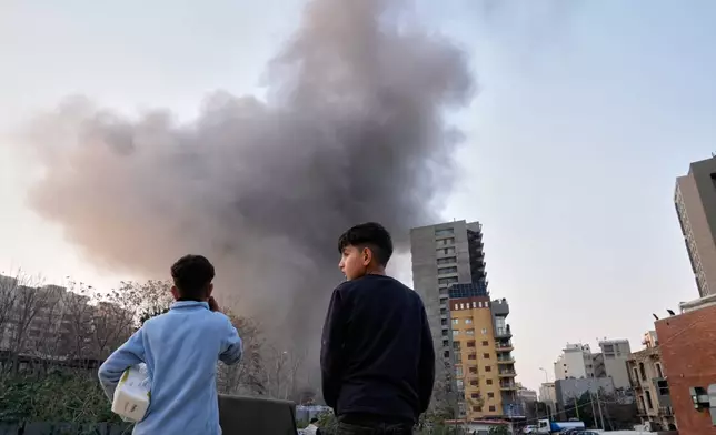 Two boys watch as smoke rises from a building nearby after an Israeli strike in central Beirut, Lebanon, Thursday, March 12, 2026. (AP Photo/Hussein Malla)
