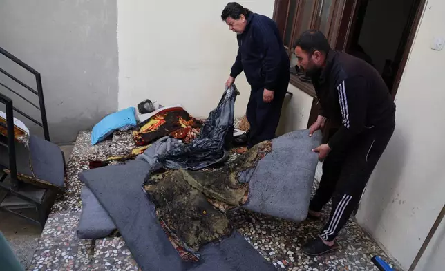 Men remove burned furniture inside a damaged home following overnight violence in the predominantly Christian town of Al-Suqaylabiyah, west of Hama, Syria, Saturday, March 28, 2026. (AP Photo/Omar Albam)