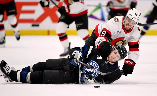 Tampa Bay Lightning defenseman J.J. Moser (90) is pulled down to the ice by Ottawa Senators right wing Drake Batherson (19) as they battle for the puck during the first period of an NHL hockey game Saturday, March 28, 2026, in Tampa, Fla. (AP Photo/Jason Behnken)