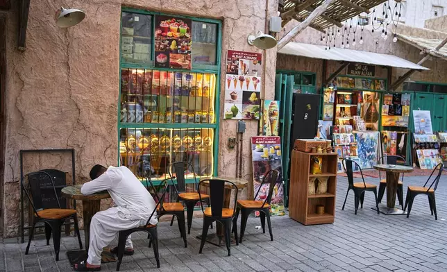 A man naps on a cafe table at the empty Al Seef market, next to the historic Al Fahidi neighborhood along Dubai Creek, one of the main tourist areas of Dubai, United Arab Emirates, Friday, March 13, 2026, as tourism slows amid regional tensions linked to the Iran war. (AP Photo/Fatima Shbair)