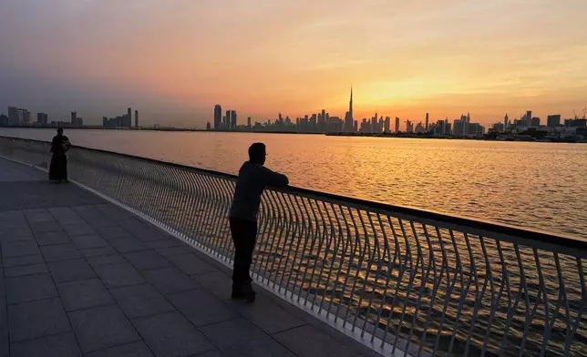 People enjoy the sunset with the view of the city skyline and Burj Khalifa, at Dubai Creek Harbour in Dubai, United Arab Emirates, Wednesday, March 11, 2026. (AP Photo/Fatima Shbair)