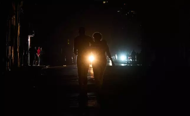 People cross a street during a blackout in Havana, Wednesday, March 4, 2026. (AP Photo/Ramon Espinosa)