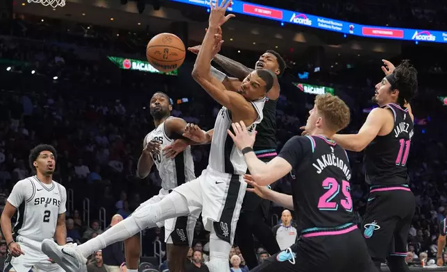 San Antonio Spurs forward Victor Wembanyama, left, front, goes for a rebound against Miami Heat forward Myron Gardner, left, rear, during the second half of an NBA basketball game, Monday, March 23, 2026, in Miami. (AP Photo/Lynne Sladky)