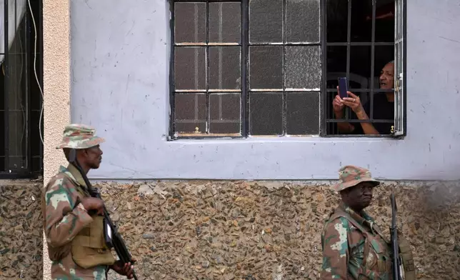 A resident uses a mobile phone to take a photograph of the South African National Defense Force officers deployed in the area, in the Riverlea township of Johannesburg, South Africa, Wednesday, March 11, 2026. (AP Photo/Themba Hadebe)