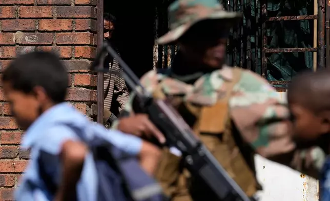 A man watches on South African National Defense Force officers patrolling the street in the Westbury township of Johannesburg, South Africa, Wednesday, March 11, 2026. (AP Photo/Themba Hadebe)