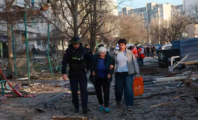 A rescuer helps an elderly woman to leave her home damaged by Russian aerial guided bomb in Zaporizhzhia, Ukraine, Saturday, March 14, 2026. (AP Photo/Kateryna Klochko)