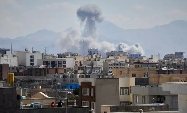 People watches from a rooftop as a plume of smoke rises after a strike in Tehran, Iran, Sunday, March 1, 2026. (AP Photo/Vahid Salemi)