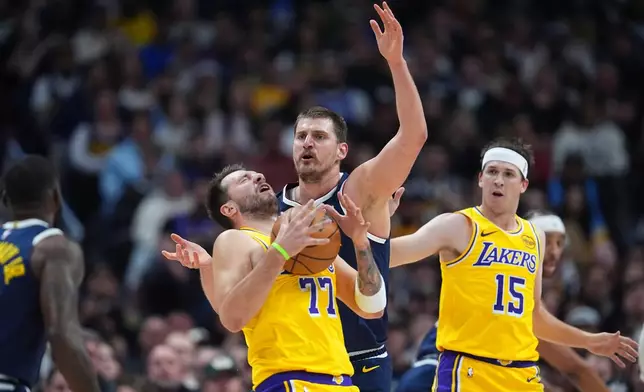 Los Angeles Lakers guard Luka Dončić, left, reacts after getting hit in the face by the ball while fighting for control with Denver Nuggets center Nikola Jokić as Los Angeles guard Austin Reaves, right, looks on in the first half of an NBA basketball game Thursday, March 5, 2026, in Denver. (AP Photo/David Zalubowski)