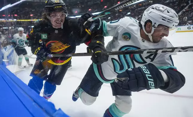 Vancouver Canucks' Curtis Douglas, left, checks Seattle Kraken's Matty Beniers during the first period of an NHL hockey game, in Vancouver, on Saturday, March 14, 2026. (Darryl Dyck/The Canadian Press via AP)