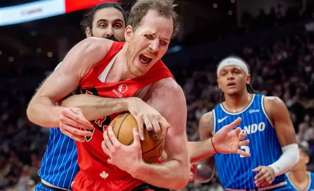 Toronto Raptors centre Jakob Poeltl (front) is fouled by Orlando Magic centre Goga Bitadze (back left) as Magic forward Paolo Banchero (right) looks on during first half NBA action in Toronto on Sunday, March 29, 2026. (Frank Gunn/The Canadian Press via AP)