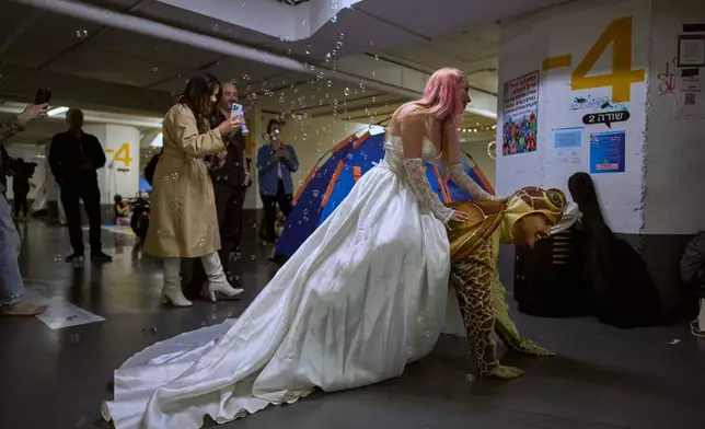 A woman dressed as a bride rides on the back of a man dressed as a turtle during a singles event in an underground parking garage used as a shelter against possible Iranian missile attacks in Tel Aviv, Israel, Tuesday, March 17, 2026. (AP Photo/Oded Balilty)