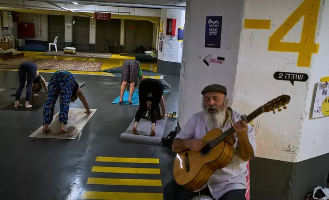 A man plays the guitar as people attend a yoga class in an underground parking garage used as a shelter against possible Iranian missile attacks in Tel Aviv, Israel, Tuesday, March 17, 2026. (AP Photo/Oded Balilty)