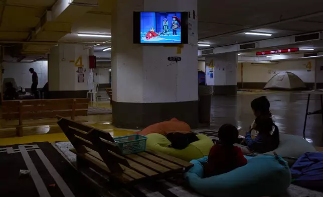 Children watch TV in an underground parking garage where people spend the night as a precaution against possible Iranian missile attacks in Tel Aviv, Israel, Thursday, March 12, 2026. (AP Photo/Oded Balilty)