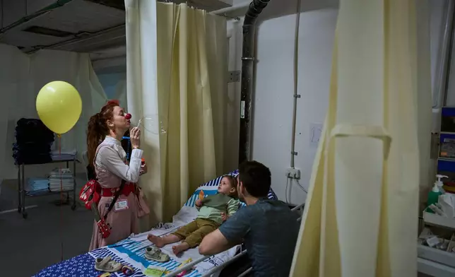 A medical staff member entertains a young patient in a temporary emergency ward set up in a parking garage used as a shelter beneath Sheba Medical Center in Ramat Gan, Israel, Tuesday, March 17, 2026. (AP Photo/Oded Balilty)