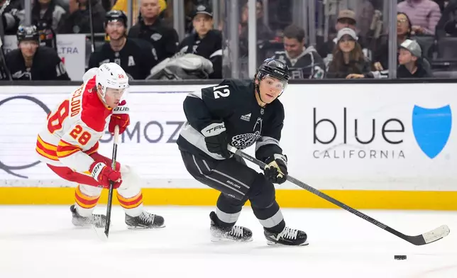 Los Angeles Kings left wing Trevor Moore, right, moves the puck past Calgary Flames defenseman Zach Whitecloud during the second period of an NHL hockey game Saturday, Feb. 28, 2026 in Los Angeles. (AP Photo/Ryan Sun)