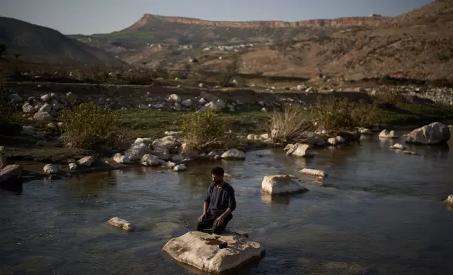 A Muslim worker prays while kneeling on a rock in a river bed as he breaks from his work at a traditional charcoal production site in Sarkand, Iraq, Thursday, March 12, 2026. (AP Photo/Leo Correa)