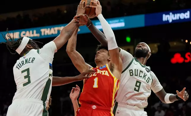 Atlanta Hawks forward Jalen Johnson (1) shoots against Milwaukee Bucks' Myles Turner (3) and Bobby Portis (9) during the second half of an NBA basketball game, Saturday, March 14, 2026, in Atlanta. (AP Photo/Mike Stewart)
